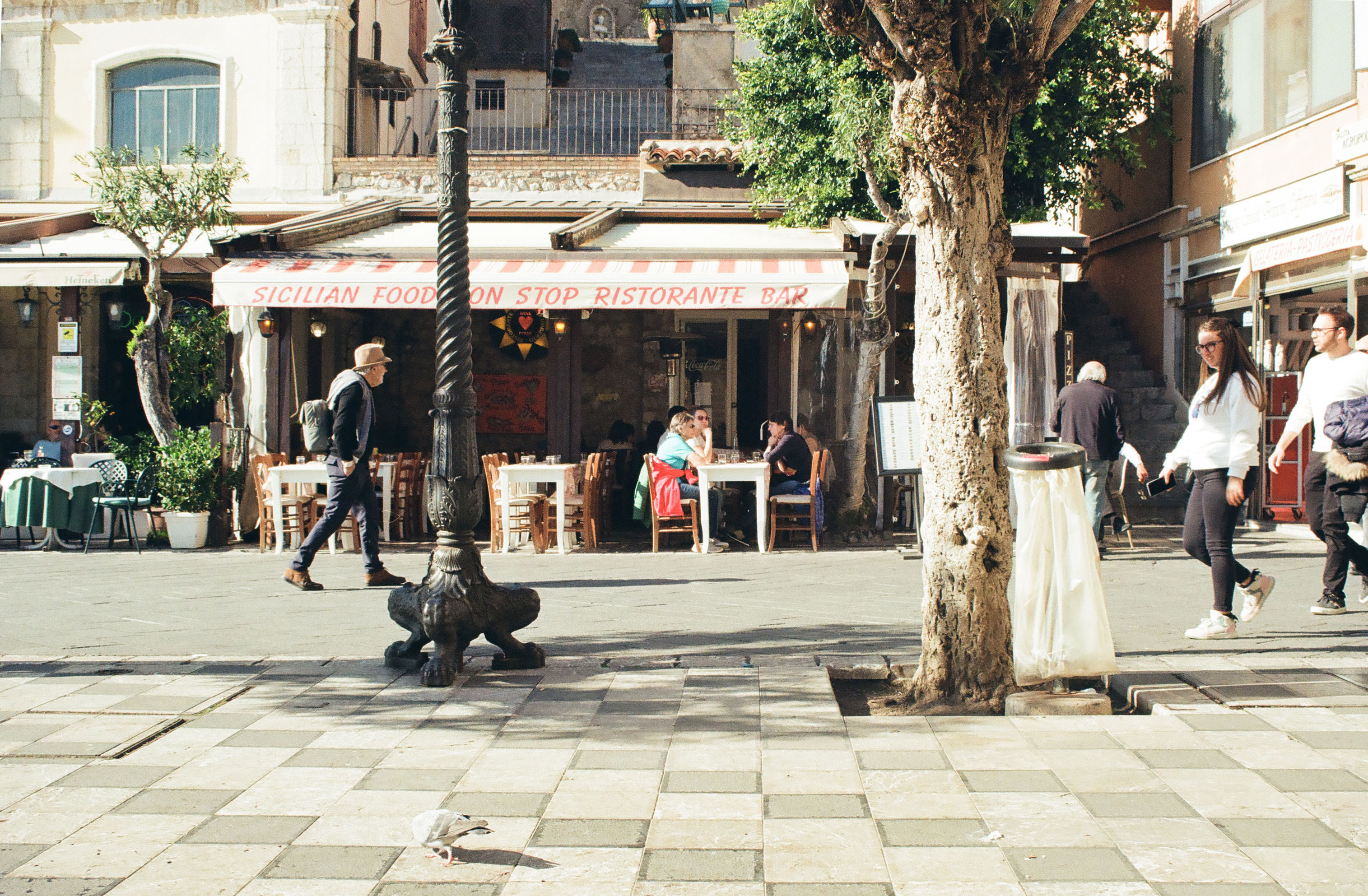 image of a man walking through the square of a town on a sunny day, restaurants and cafes in the background